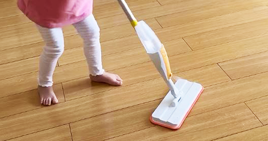 Young girl spraying water from Quiggly’s kid-sized spray mop onto a hardwood floor