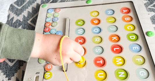A kid's hand using the magnetic want to sort letters in the magnetic Montessori-inspired alphabet & color maze board