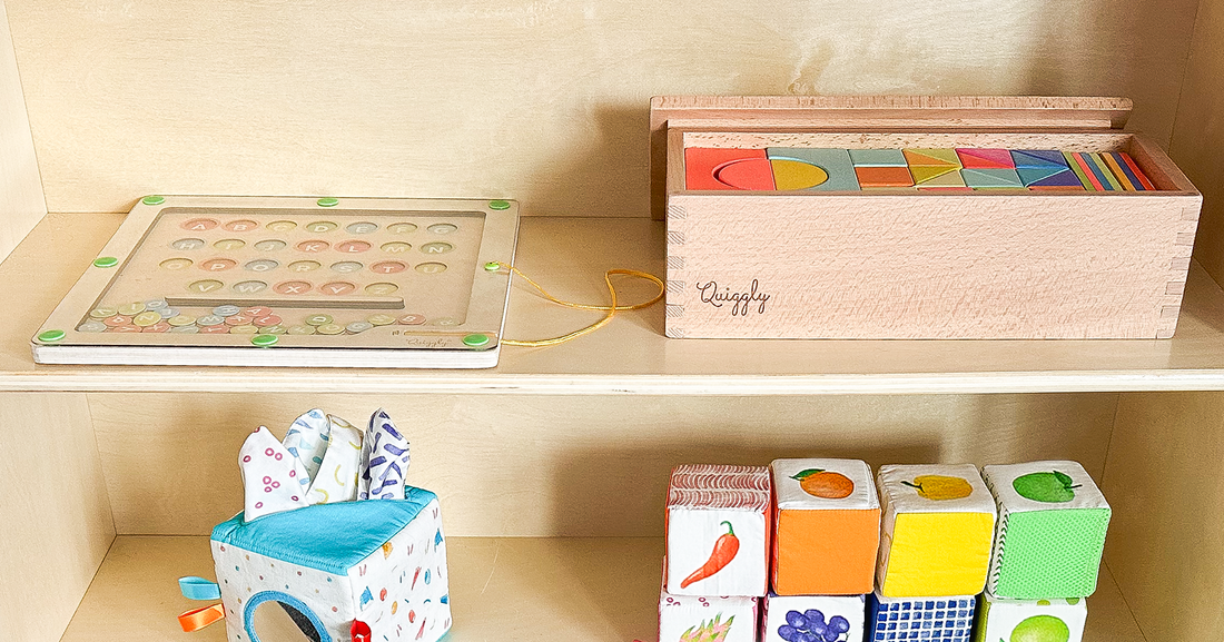Montessori-themed shelf setup with Quiggly’s magnetic maze, rainbow wooden blocks in an open box, toy tissue box, and soft fabric block set