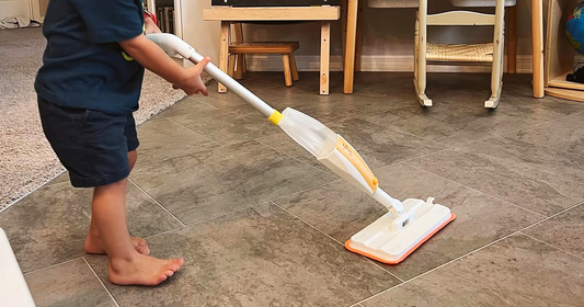 Young child wiping floors with Quiggly’s toy spray mop - a great cleaning tool for toddlers & kids