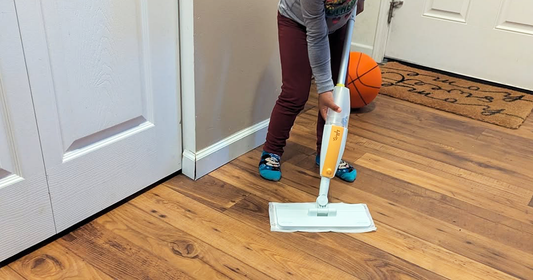 Child inspecting the spray bottle of Quiggly’s toy mop while using a disposable cloth as a mop pad