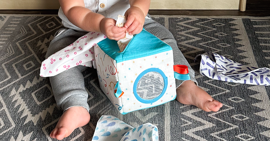 Baby pulling tissues out of Quiggly's soft fabric tissue box toy