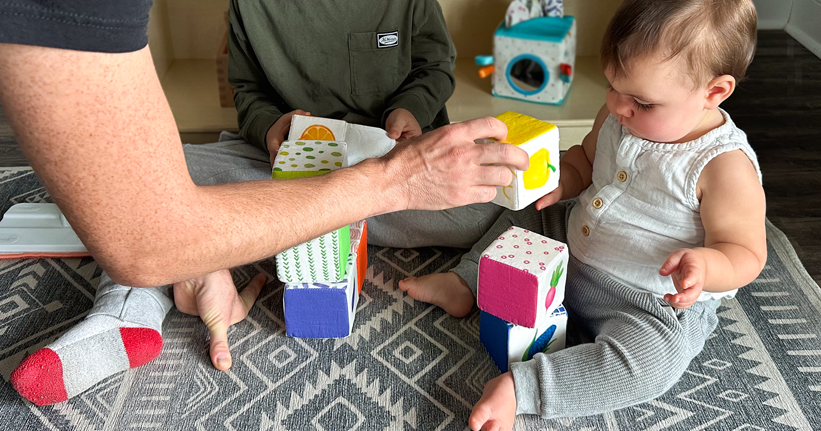 Father & son helping baby stack Quiggly's Soft Fabric Rainbow Blocks