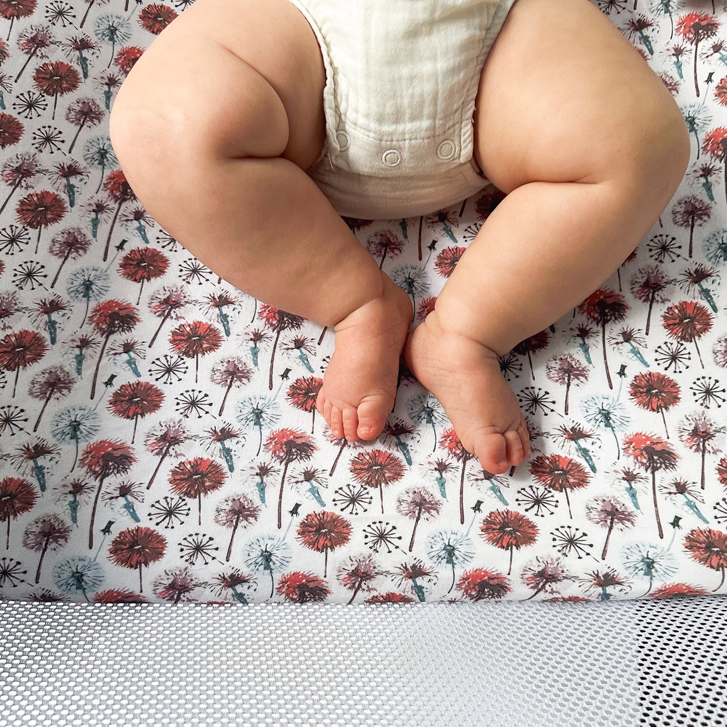Baby lying comfortably on dandelion-patterned organic sheet inside Guava Lotus bassinet crib