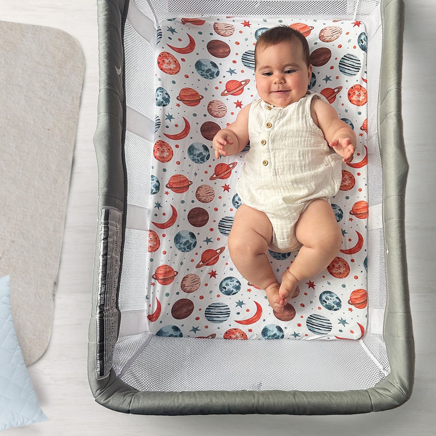 Smiling baby lying on space-patterned bassinet sheet inside Guava Lotus bassinet crib