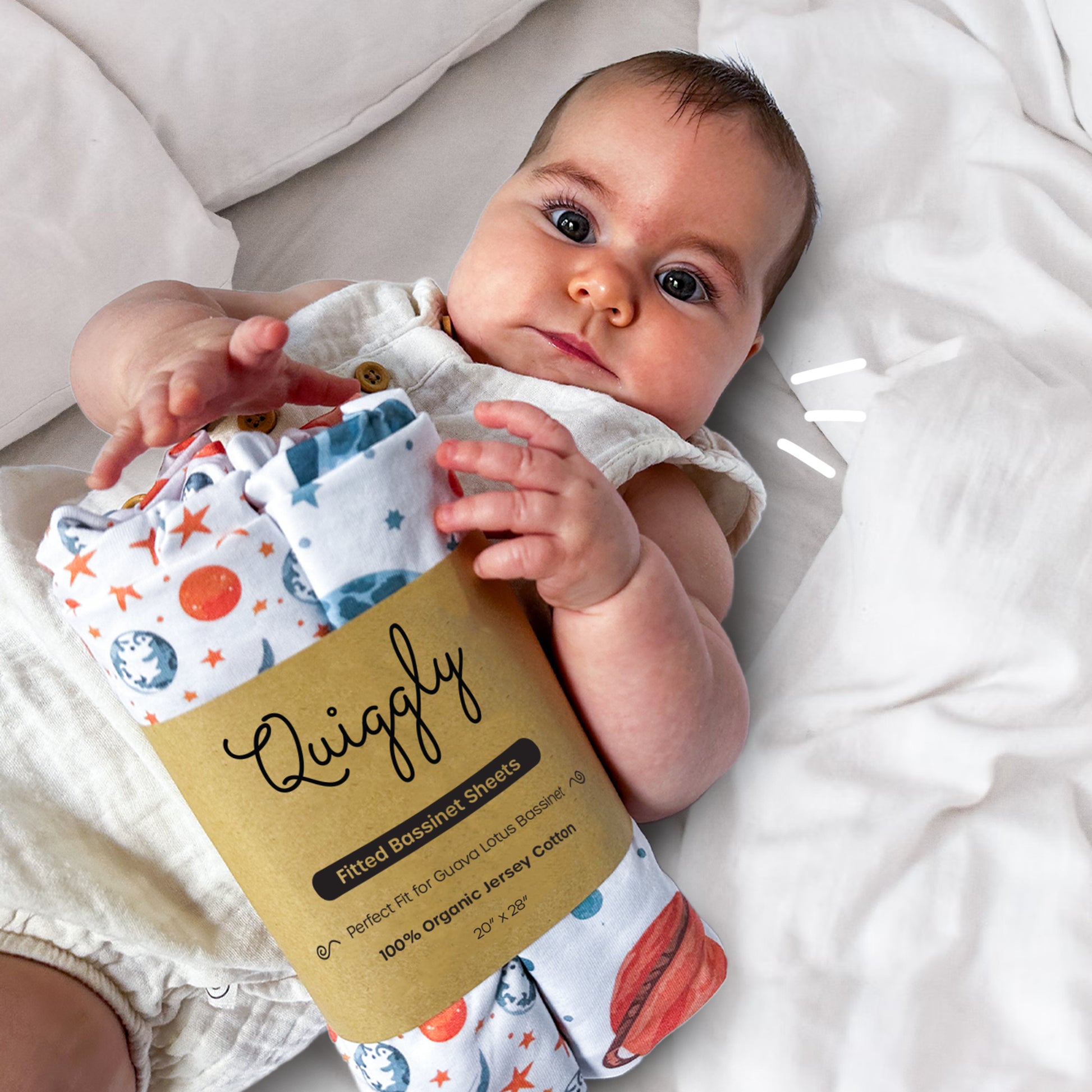 Baby holding a 2-packed bassinet crib sheet in Starry Slumber theme