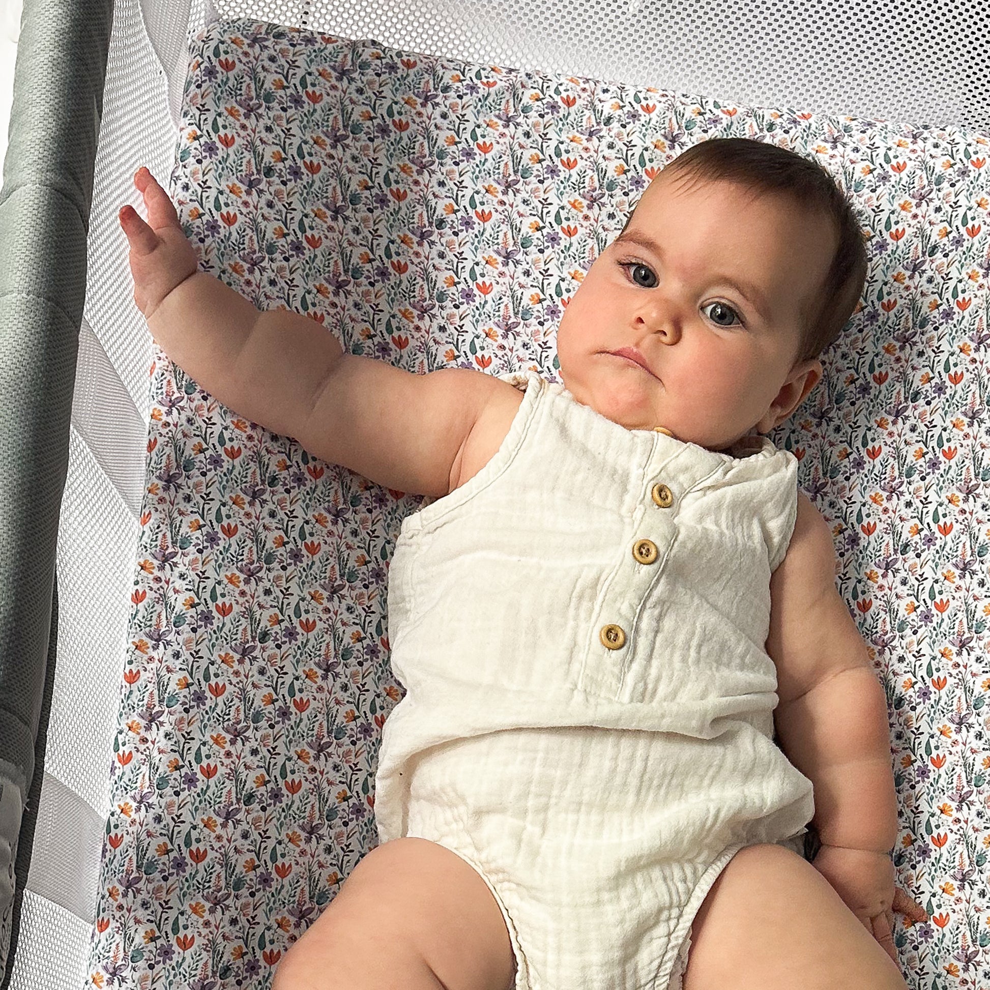 Baby lying comfortably on floral-patterned bassinet crib sheet inside Guava Lotus bassinet crib