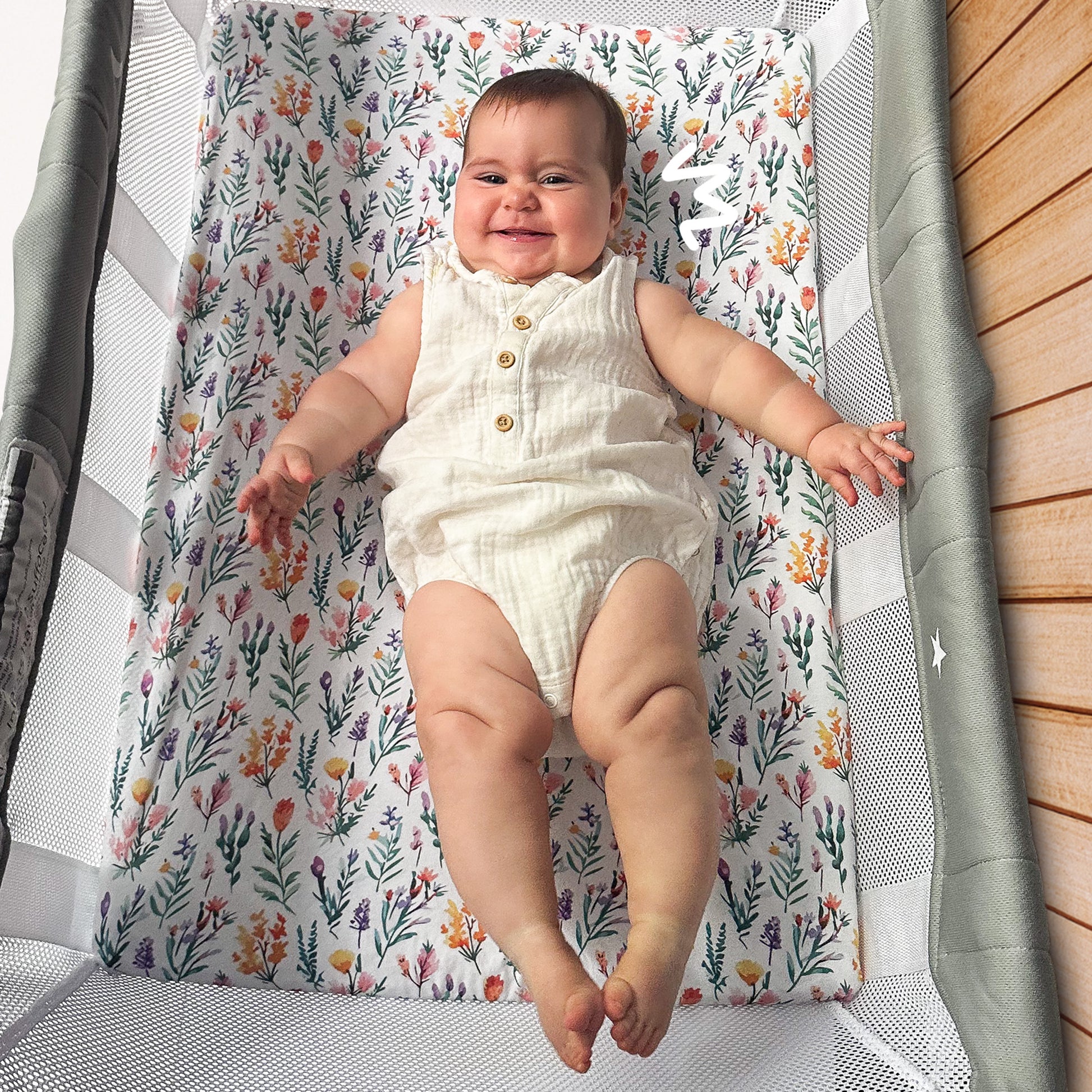 Baby playing comfortably inside Guava Lotus bassinet crib on Quiggly’s soft organic cotton sheet