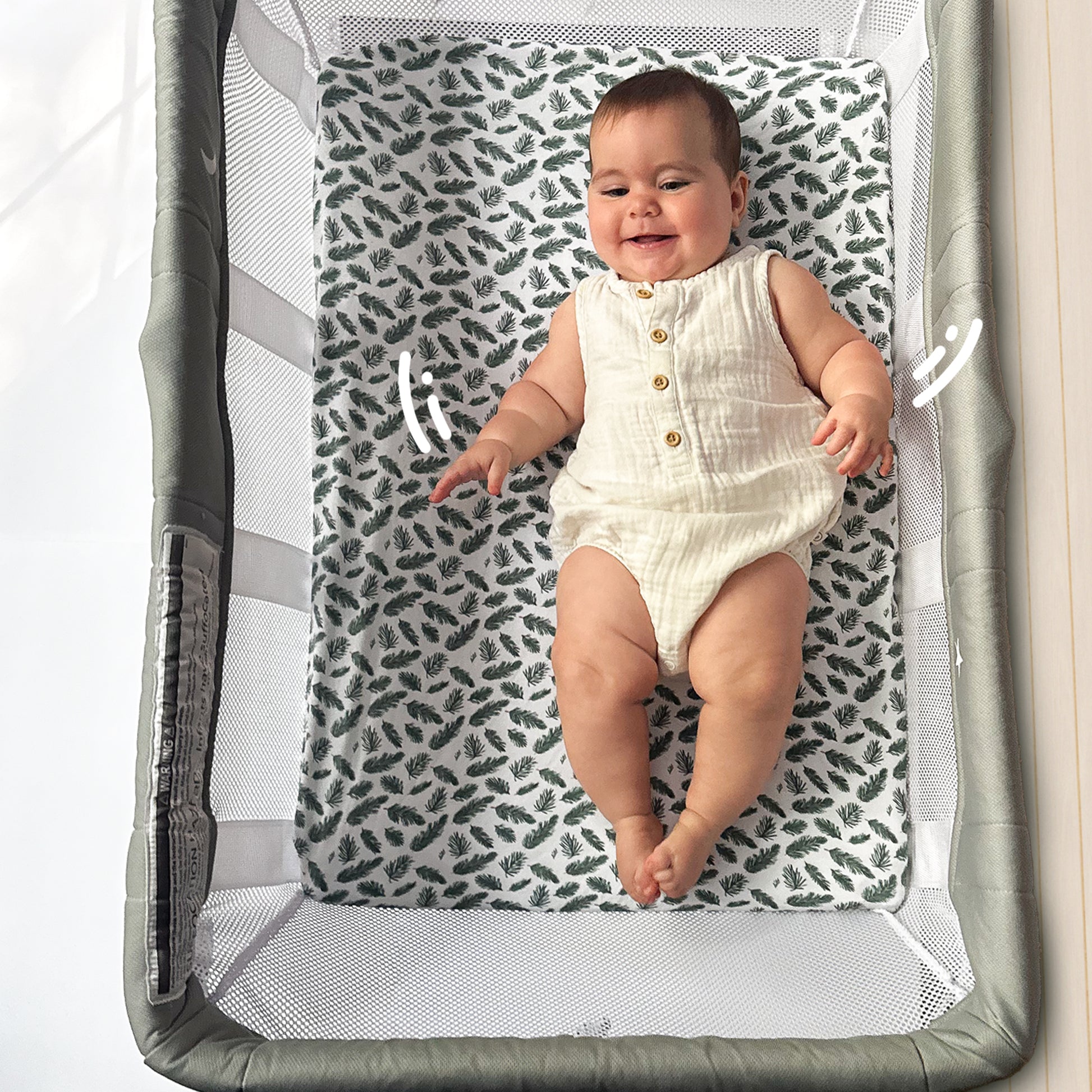 Smiling baby lying on leaf-patterned bassinet crib sheet inside Guava Lotus bassinet crib