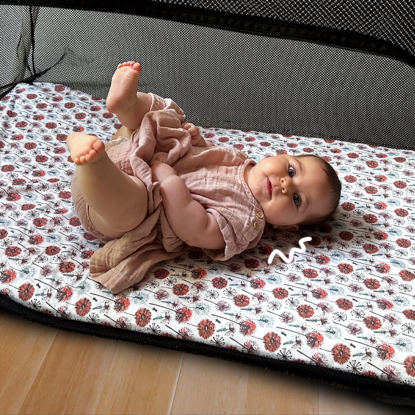 Baby playing comfortably inside Guava Lotus travel crib on Quiggly’s soft organic cotton sheet