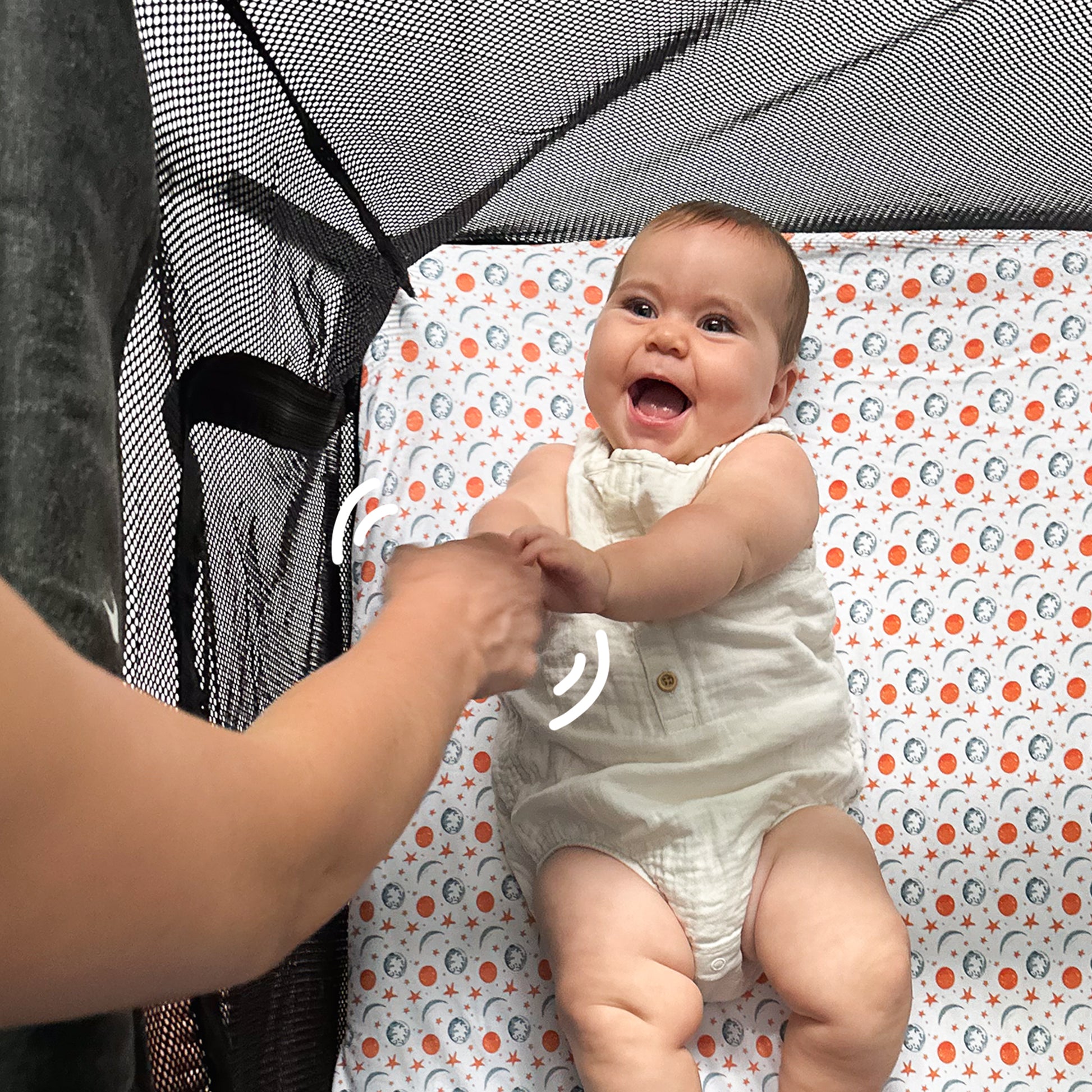 Baby playing comfortably inside Guava Lotus travel crib on Quiggly’s soft organic cotton sheet