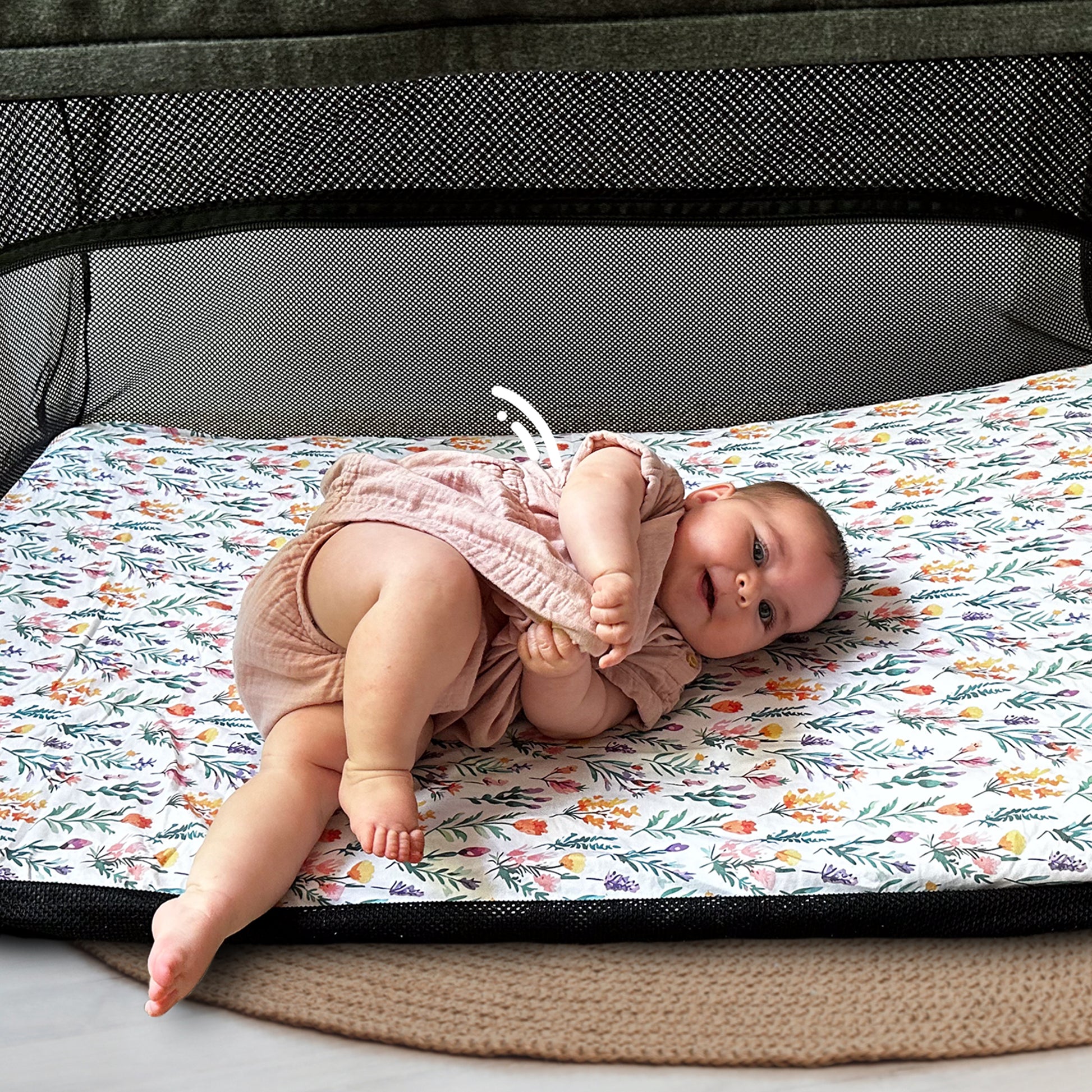 Baby playing comfortably inside Guava Lotus travel crib on Quiggly’s soft organic cotton sheet