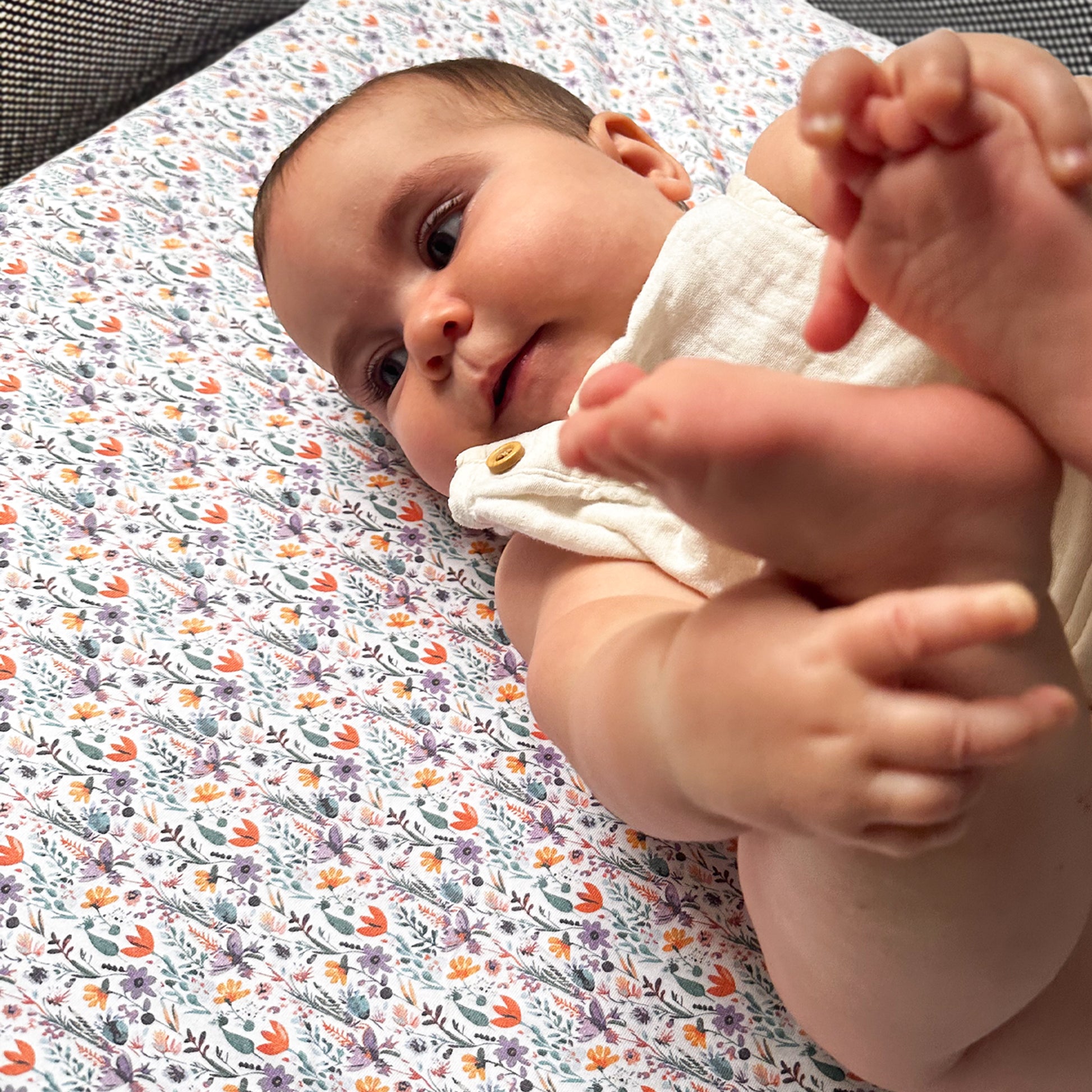 Baby lying on floral-patterned travel crib sheet inside Guava Lotus travel crib
