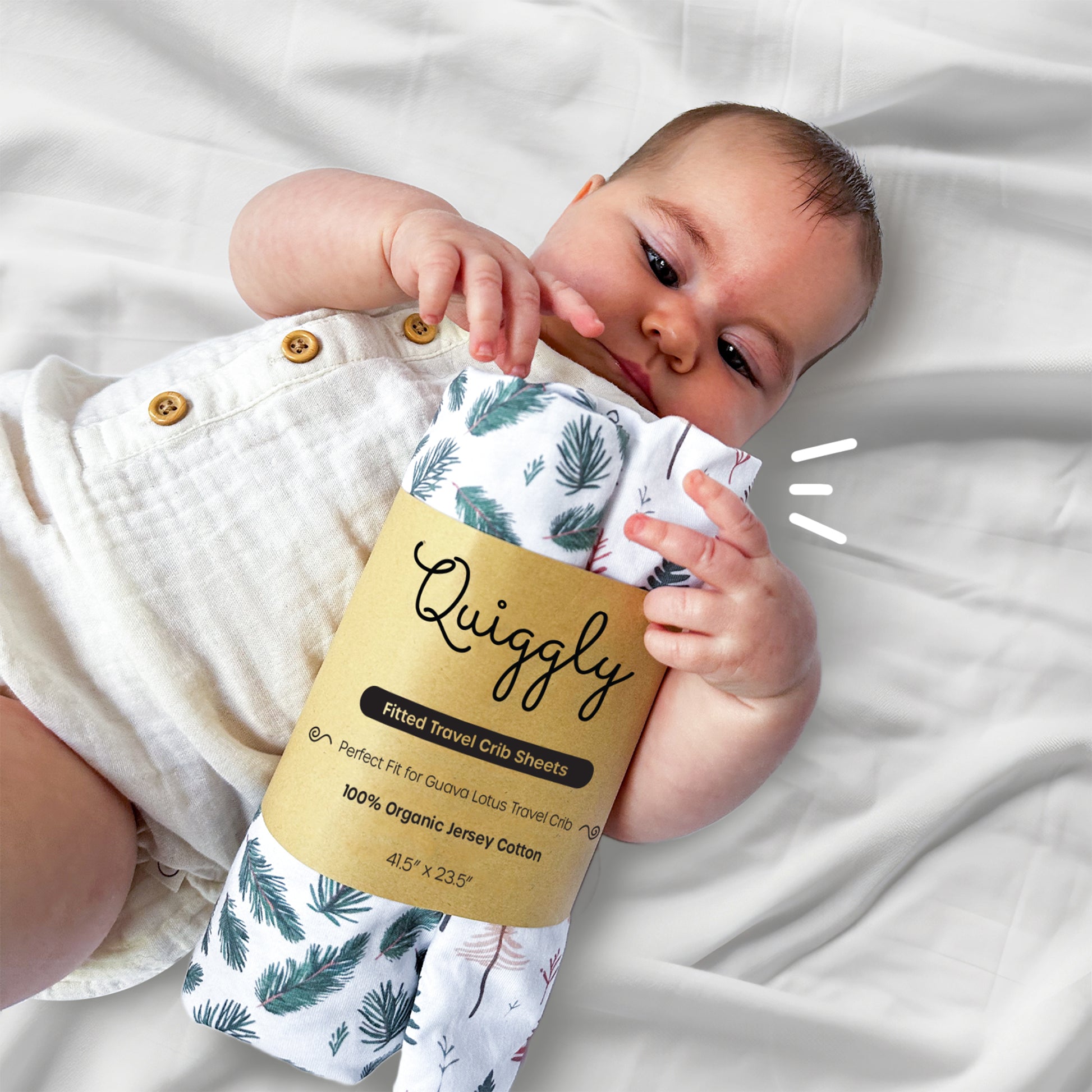 Baby holding a 2-packed travel crib sheet in Whispering Woodland theme