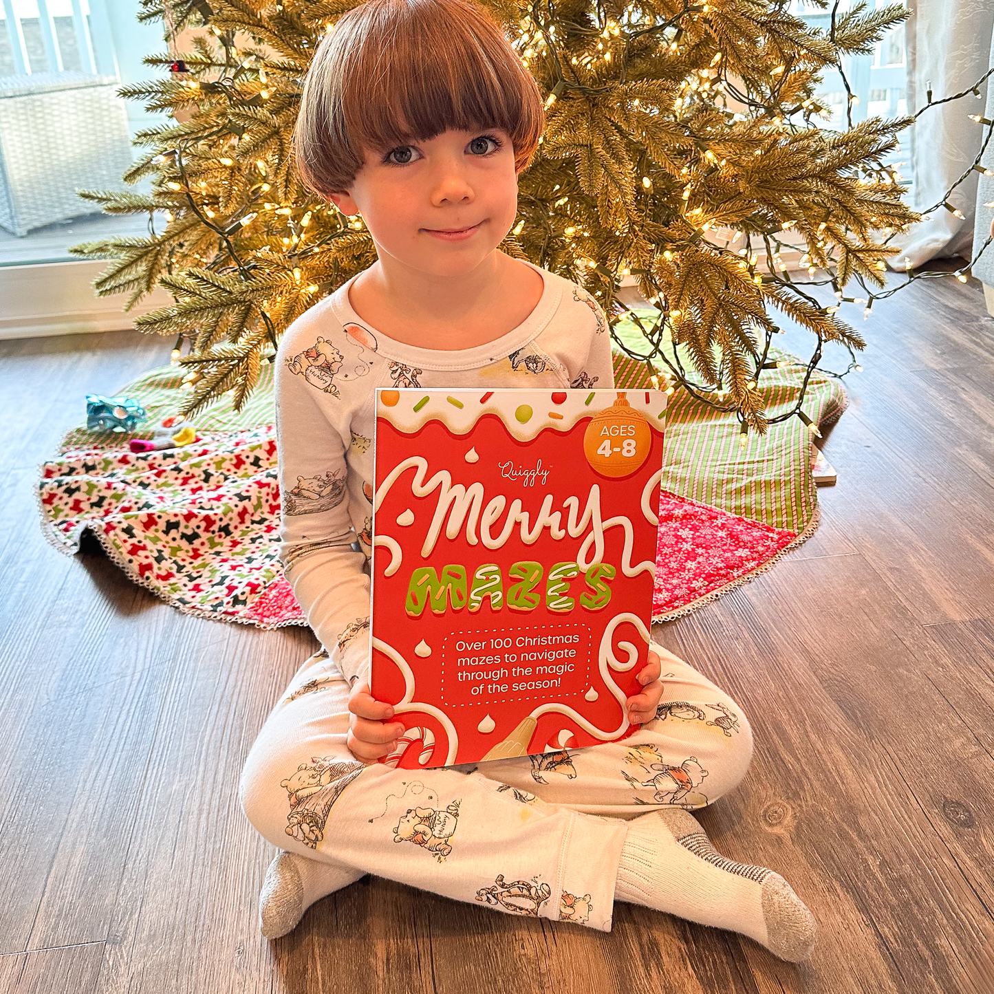 Child holding Quiggly Merry Mazes book with a decorated Christmas tree in the background