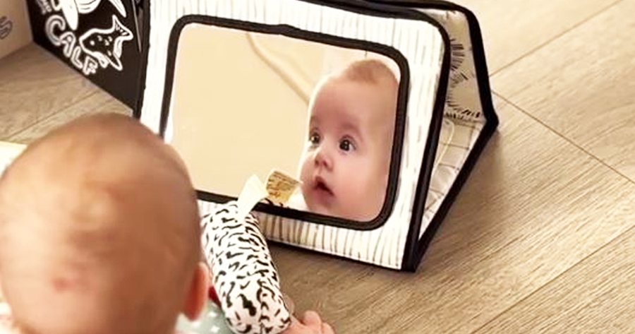 Baby looking at a baby-safe mirror propped up by a high-contrast patterned stand for tummy time