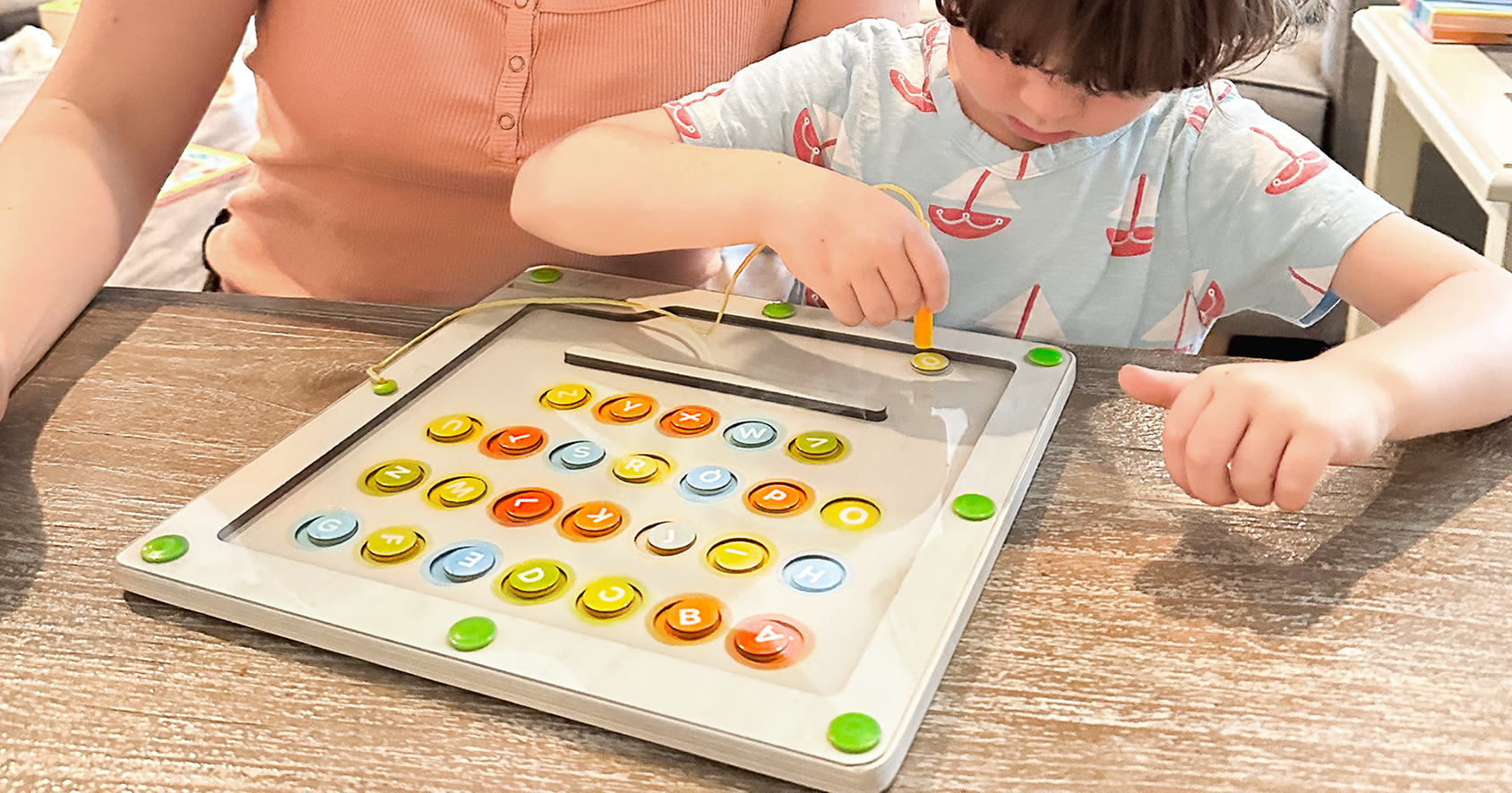 Young boy using a magnetic wand to move alphabet pieces on Quiggly’s wooden alphabet & color maze board