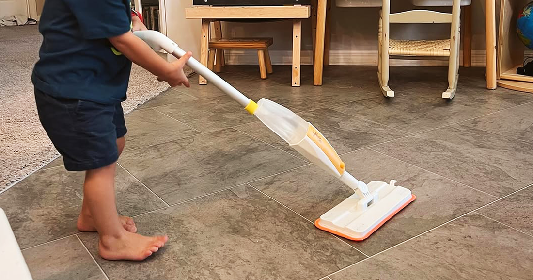 Young child wiping floors with Quiggly’s toy spray mop - a great cleaning tool for toddlers & kids