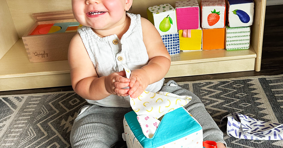 Cheerful baby grabbing beautifully designed soft fabric tissues from Quiggly’s tissue box toy