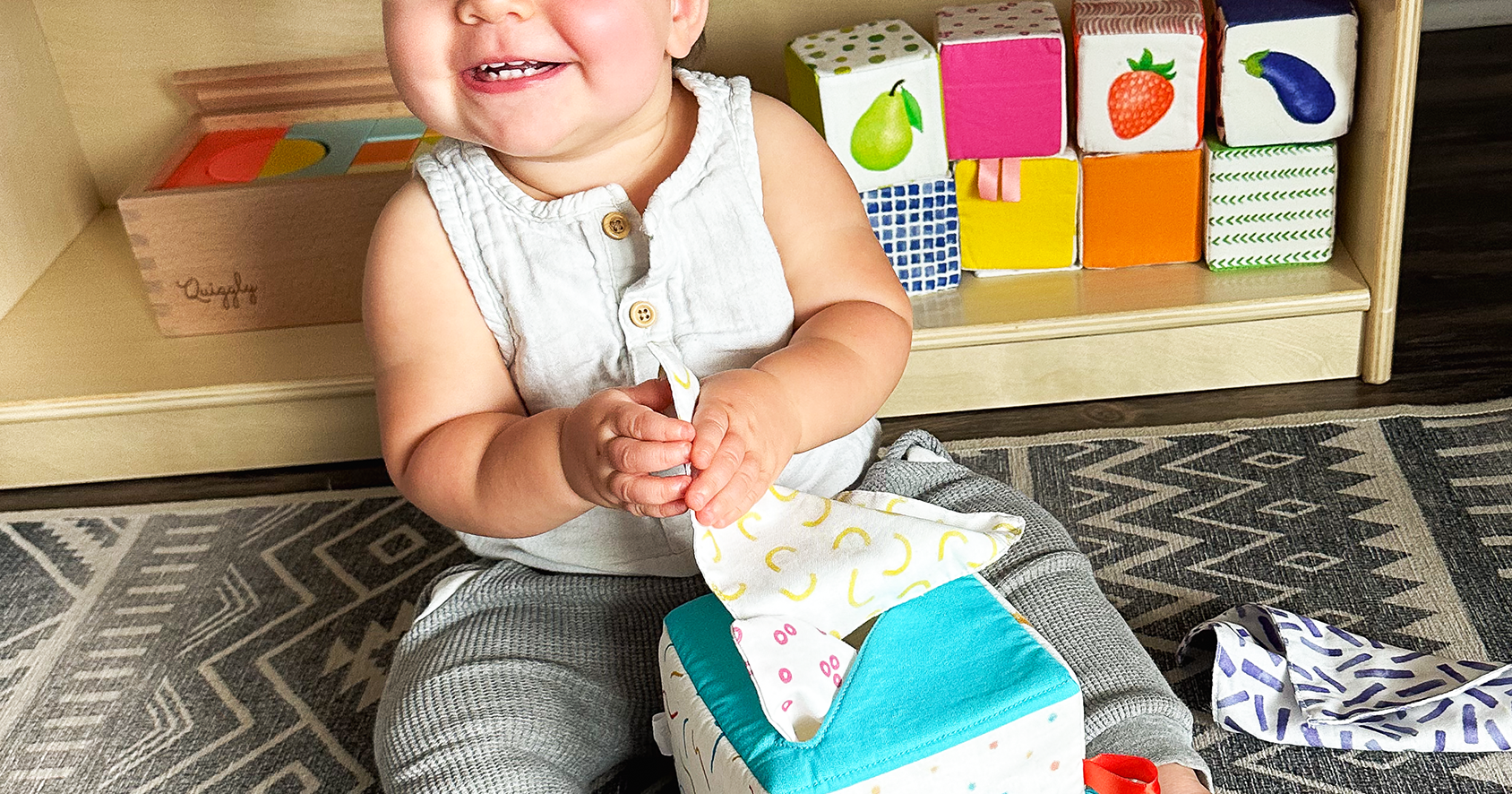 Cheerful baby grabbing beautifully designed soft fabric tissues from Quiggly’s tissue box toy