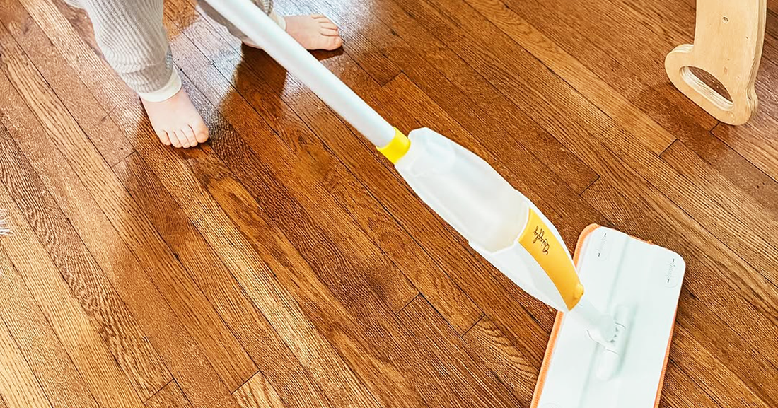 A young child using a real spray toy mop on a wooden floor
