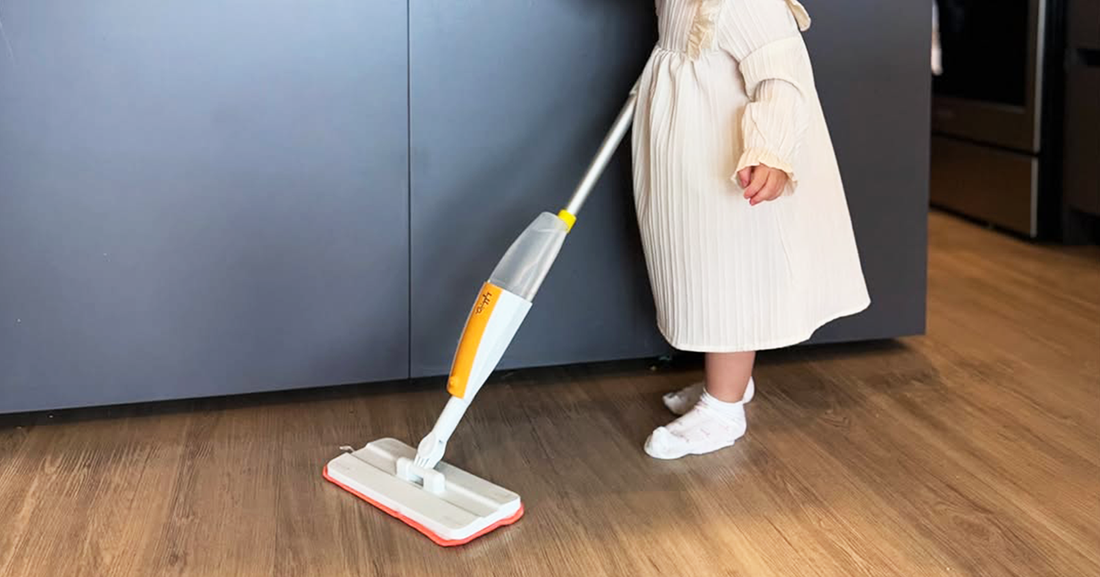 A toddler using a kid-sized real cleaning tool on a wooden floor