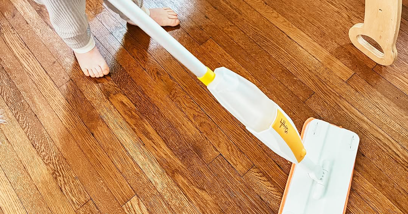 A young boy using a real spray toy mop on a wooden floor