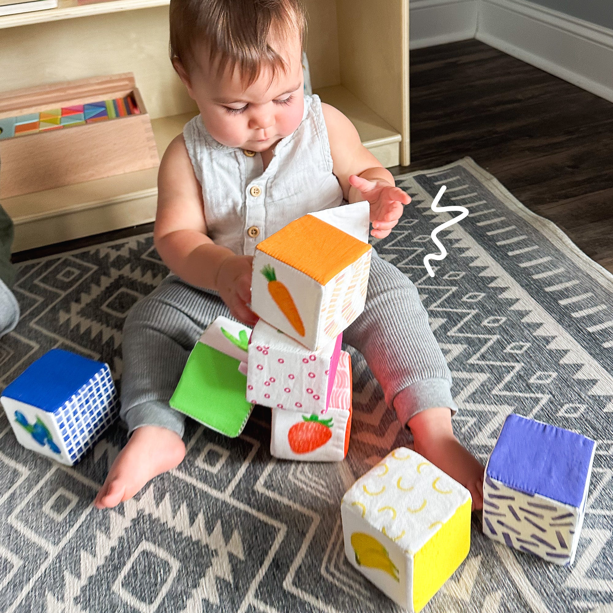 Baby discovering a flap feature on fabric block while attempting to stack soft blocks