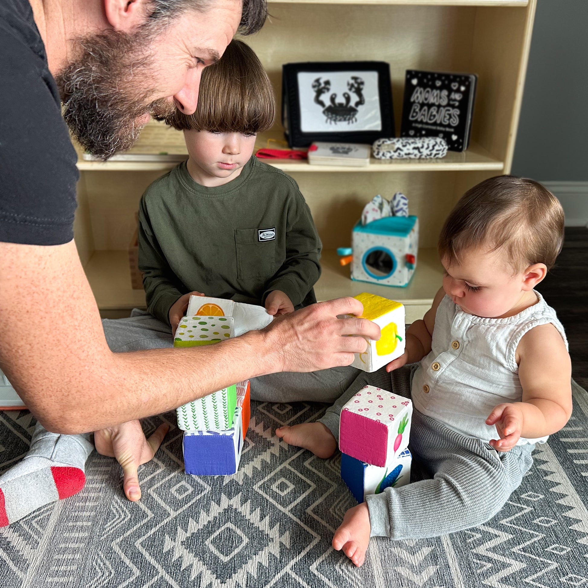 Father and son playfully helping baby stack rainbow fabric blocks during bonding time