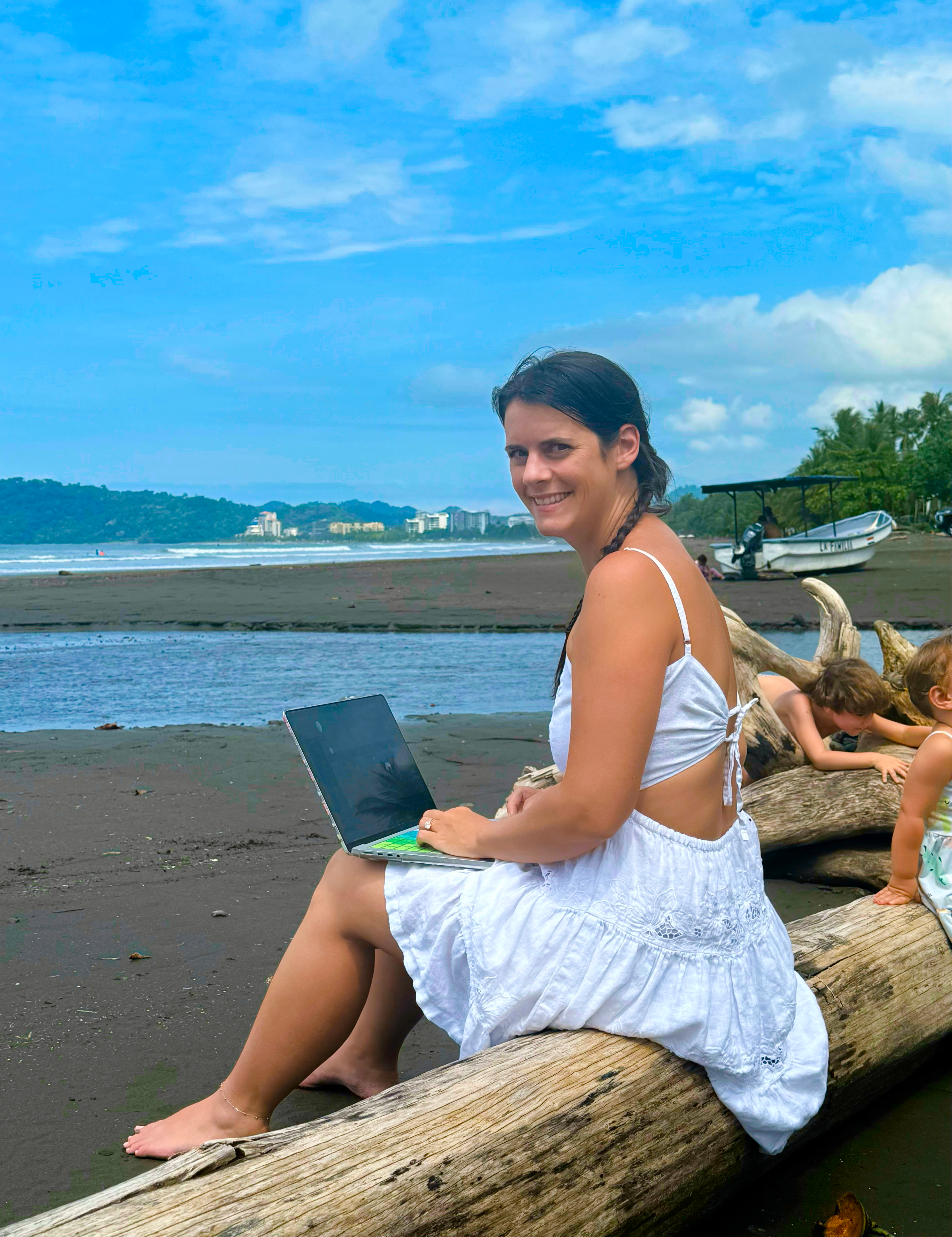 Quiggly founder working on laptop by the beach while her children play in the background