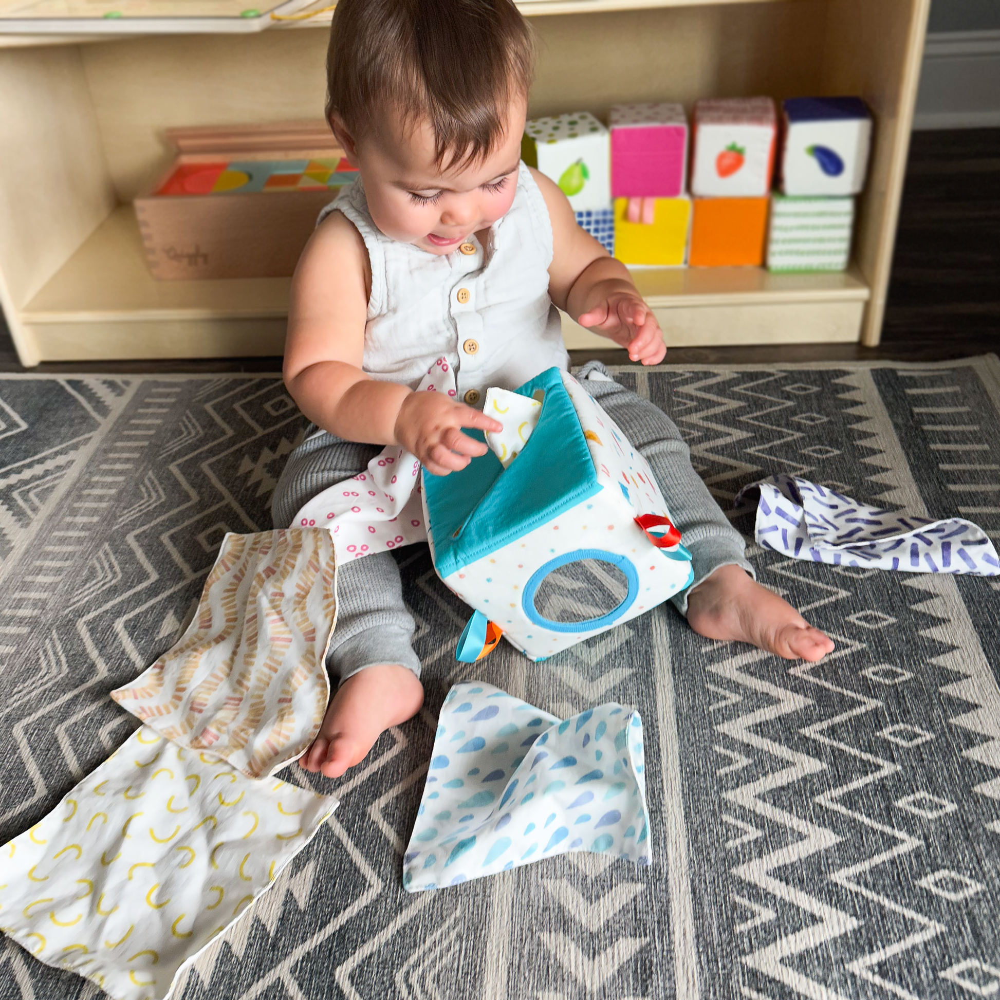 Baby joyfully tugging a tissue cloth from soft fabric tissue box during sensory playtime