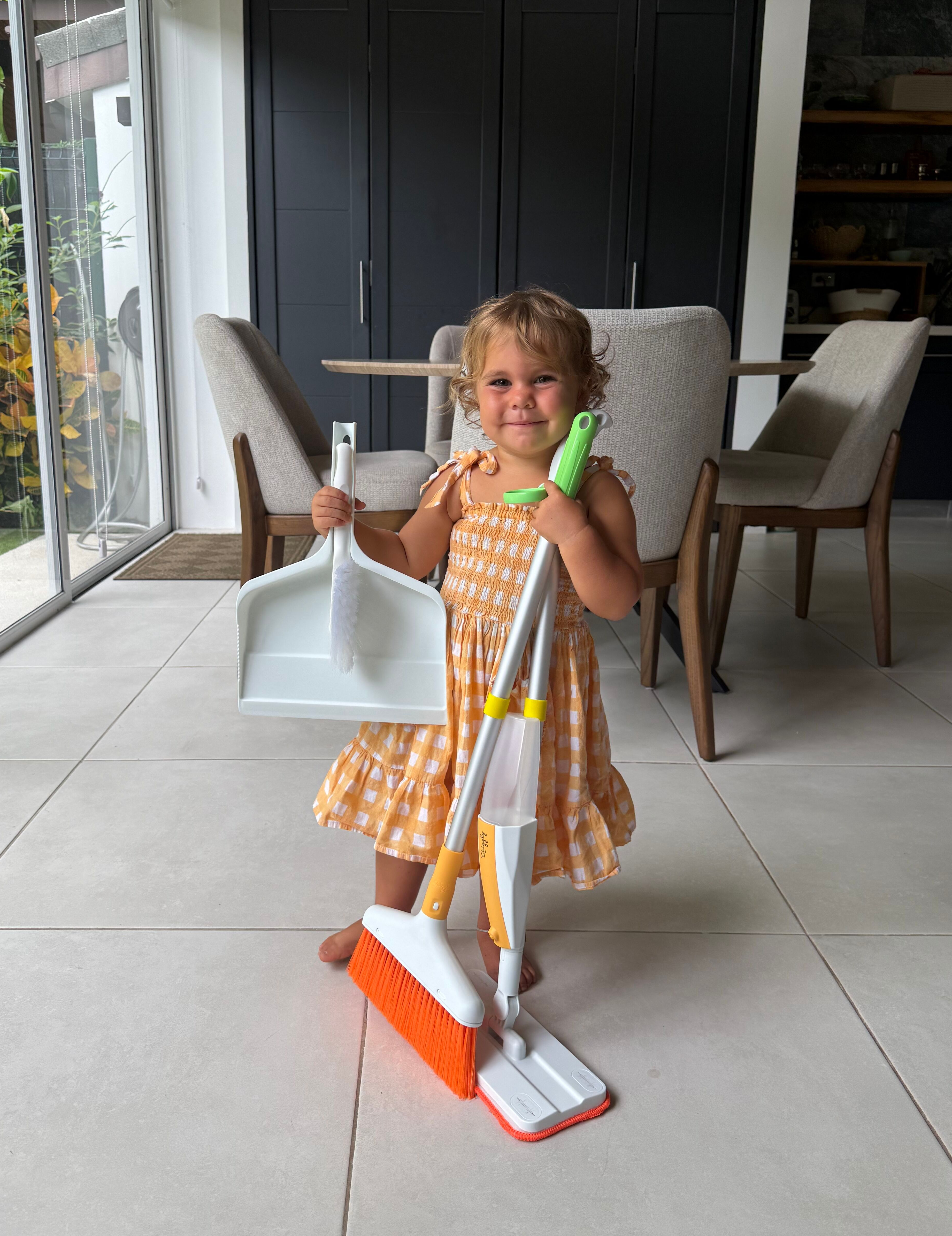 3 year old child holding Quiggly toddler cleaning set with real spray mop, broom, dustpan, and small brush