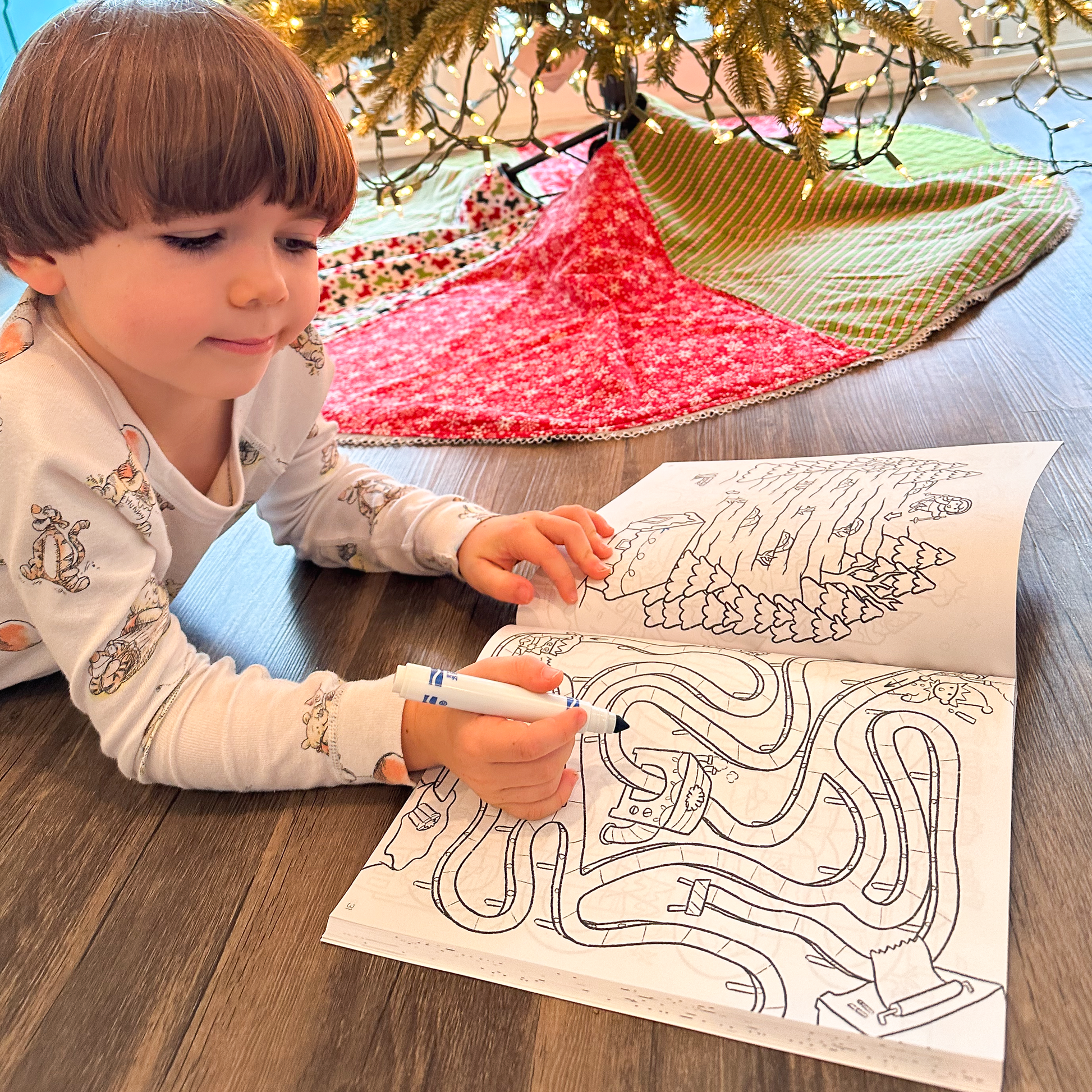 Kid solving a festive maze puzzle under the Christmas tree from Quiggly Merry Mazes activity book